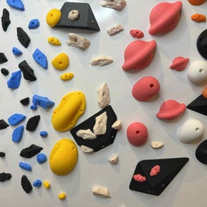 Peut inclure: Un ensemble de prises d'escalade colorées de différentes formes et tailles, comprenant du noir, du bleu, du jaune, du rose et du blanc. Les prises sont conçues pour l'escalade et le bloc en salle, avec diverses textures et options de prise.