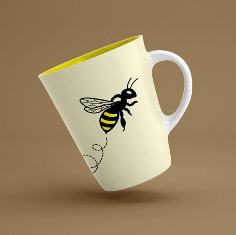 May include: A light yellow ceramic mug featuring a graphic of a black and yellow bee in flight. The bee is positioned above a dashed, swirling black line representing its flight path. The mug has a white handle and a bright yellow interior.