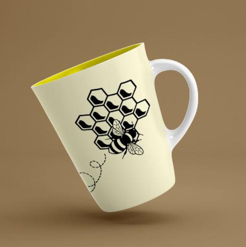 May include: Cream-colored ceramic mug with a yellow interior and a white handle. The mug features a black graphic of a honeycomb and a bee. A dotted line trails from the bee, suggesting movement. The mug is angled, showcasing its design.