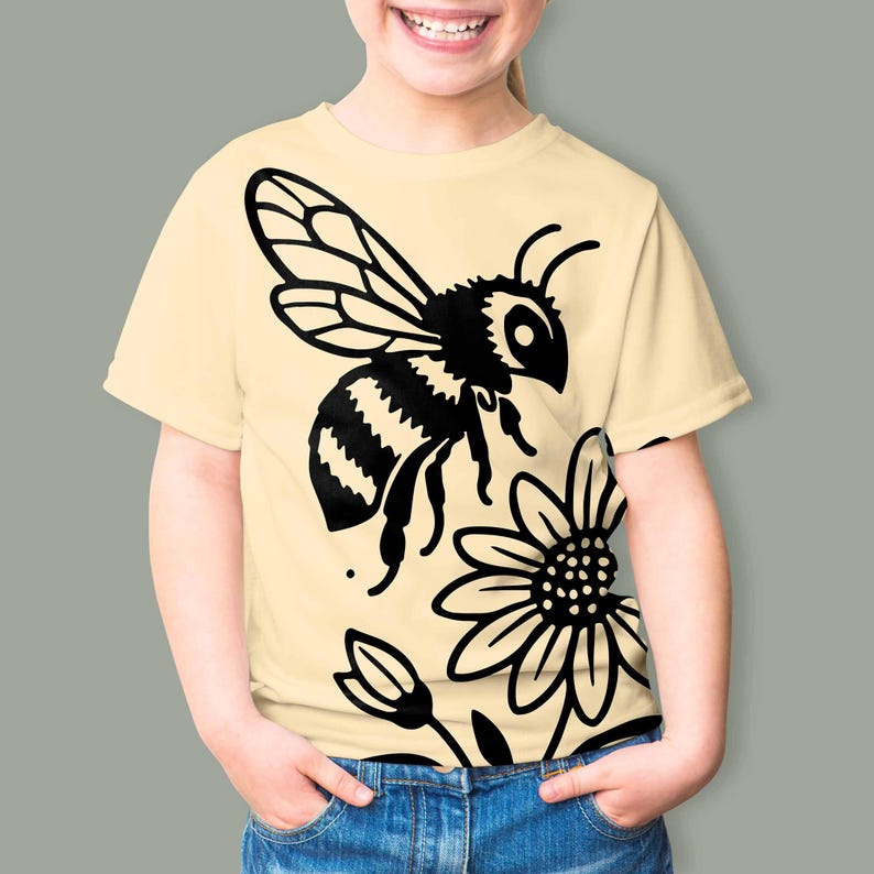 May include: A light yellow short-sleeve t-shirt featuring a large black graphic print of a bee in flight above a daisy flower. The design is centered on the front of the garment, showcasing a bold, high-contrast illustration of the insect.