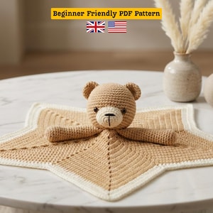 Può includere: Una coperta di sicurezza a forma di orsetto all'uncinetto nei colori beige e crema. L'orsetto ha un viso dettagliato ed è attaccato a una coperta a forma di stella. Il testo "Beginner Friendly PDF Pattern" è nella parte superiore dell'immagine.