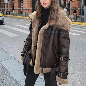 Puede incluir: Chaqueta de cuero marrón con cuello y forro de borrego. La chaqueta tiene múltiples hebillas, cierre de cremallera y cinturón. Un estilo clásico, ideal para el frío.