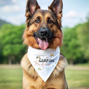 May include: A white triangular dog bandana featuring the text "Camping Buddy" in dark gray and orange script. The fabric is decorated with small illustrations of campers, pine trees, and mountains in muted earth tones, worn by a German Shepherd.