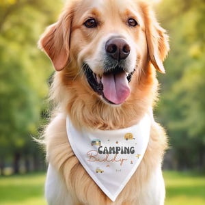 May include: A golden retriever wearing a white triangular pet bandana featuring the text "Camping Buddy" in dark brown and orange lettering, surrounded by small graphic illustrations of campers, a campfire, a rainbow, and a yellow vehicle.