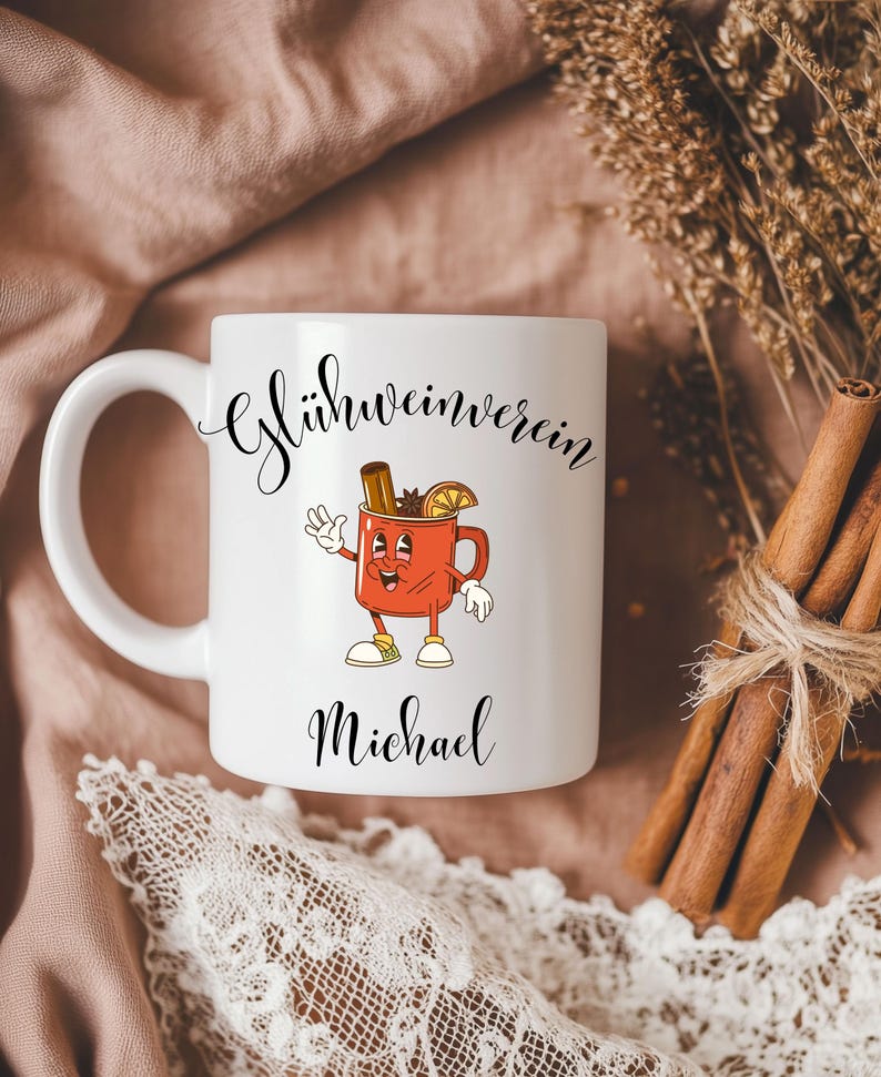 Pu&ograve; includere: Tazza in ceramica bianca con un'illustrazione a cartoni animati di una tazza rossa con un bastoncino di cannella, anice stellato e una fetta d'arancia. La tazza ha il testo "Gl&uuml;hweinverein" e "Michael" in corsivo nero.