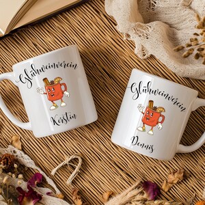 Pu&ograve; includere: Due tazze in ceramica bianca con la scritta "Gl&uuml;hweinverein" in corsivo. Ogni tazza presenta un'immagine a cartoni animati di una tazza rossa con un bastoncino di cannella e una fetta d'arancia. Una tazza &egrave; personalizzata con il nome "Kerstin", l'altra con "Dennis".