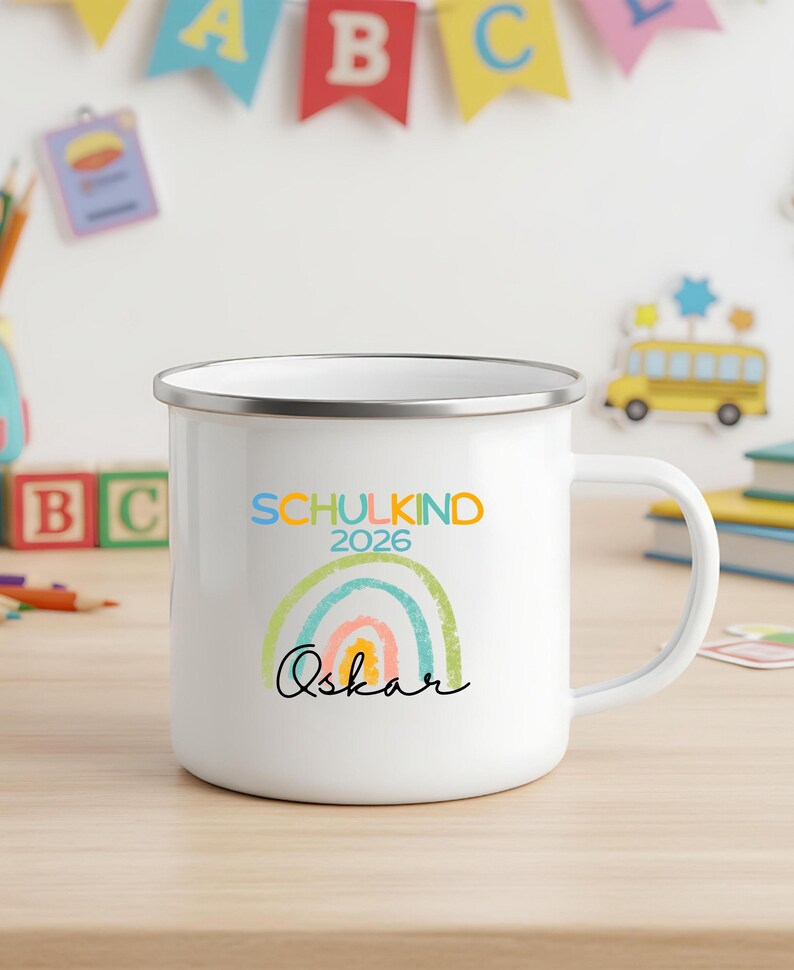May include: A white enamel mug with a silver rim featuring a colorful rainbow graphic, the text "SCHULKIND 2026" in blue and orange, and the name "Oskar" written in black cursive script across the front of the mug.