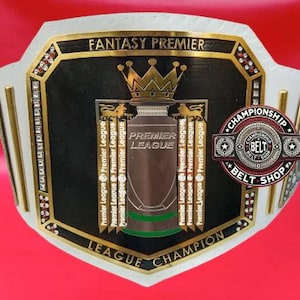 Könnte beinhalten: Ein Meisterschaftsgürtel mit schwarzem Mittelteil, goldenen Verzierungen und weißen Seiten. Das Design zeigt eine Trophik, die Worte "Premier League" und "Fantasy Premier League Champion". Ein "Championship Belt Shop" Logo ist zu sehen.