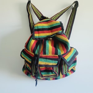 May include: A colorful backpack with a striped pattern in red, yellow, green, and black. The backpack has a flap closure, two front pockets, and adjustable shoulder straps. The bag is made of a woven fabric.