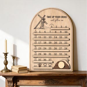 May include: Wooden religious wall decor with the text "TAKE UP YOUR CROSS and follow me." The arched sign features a cross, a figure carrying a cross, and numbered slots for tracking. The sign is made of light-colored wood.