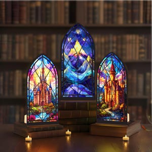May include: Three stained glass window panels depicting castles and mountain scenes. The panels are illuminated from behind, creating a warm glow. Each panel is set on a stack of books, with small candles in front.
