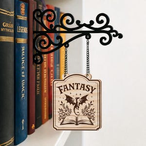 May include: A wooden sign with the word "FANTASY" and a dragon illustration, hanging from a black metal bracket. The sign is suspended by chains and is displayed in front of a bookshelf with various book titles.