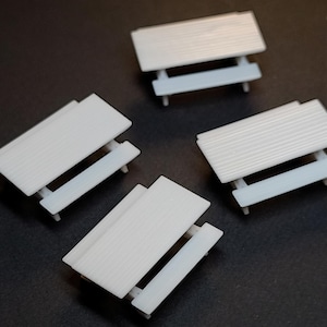 May include: Four miniature white picnic tables with a slatted tabletop design. The tables have a light gray base and are arranged on a dark surface. The image includes the text "Max Miniatures".