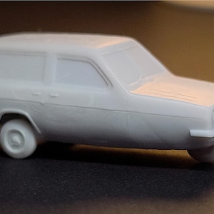 Puede incluir: Una maqueta gris clara de un coche familiar clásico. El vehículo en miniatura presenta ventanas, ruedas y líneas de carrocería detalladas, capturando la esencia del diseño original. El modelo mide aproximadamente 10 cm de largo.