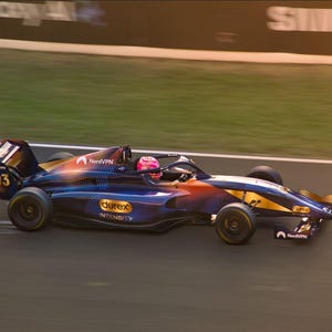 Könnte beinhalten: Ein Formel-Rennwagen in Bewegung, mit blauem, orangefarbenem und gelbem Farbschema. Das Auto hat die Nummer 03 und Sponsorenlogos. Ein Fahrer mit rosa Helm ist zu sehen. Das Auto befindet sich auf einer Rennstrecke.