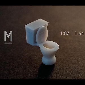 Könnte beinhalten: Eine kleine, hellblaue Miniaturtoilette mit offenem Deckel. Das Modell ist detailliert und scheint aus Kunststoff zu sein. Das Bild enthält den Text "1:87 | 1:64" und ein Logo mit dem Buchstaben "M".