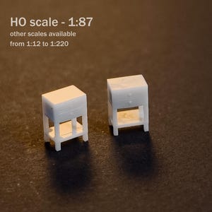 May include: Two miniature white bedside tables with two drawers and an open lower shelf. The text on the image reads M HO scale - 1:87 other scales available from 1:12 to 1:220. These small furniture pieces are designed for scale modeling projects.