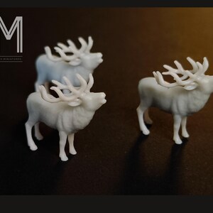May include: Three small, white elk figurines with detailed antlers are displayed against a dark background. The elk are in various poses, with one appearing to be mid-call. The image includes the text "M" and "MAX MINIATURES".