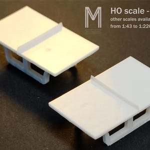 May include: Two white plastic model bridge sections with a flat rectangular top and a support structure underneath. The text on the image reads: M HO scale - 1:87 other scales available from 1:43 to 1:220. These components are designed for model building.