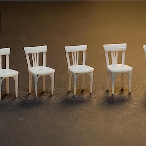 May include: Five miniature white chairs with a classic design are arranged in a row. Each chair has a slatted back and four legs. The chairs are set against a brown background, creating a simple, clean aesthetic.