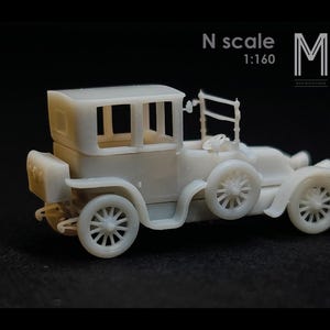 以下が含まれることがあります： オフホワイトの小さなヴィンテージカーの模型。 車はクローズドトップ、スポークホイール、詳細なフェンダーを備えています。 「N scale 1:160」の文字が見えます。 暗い背景に設定されたモデル。