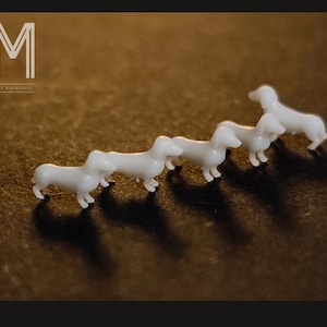 May include: A collection of small, white dachshund figurines arranged in a row, casting long shadows on a brown surface. The image includes the text "M" and "MAX MINIATURES".