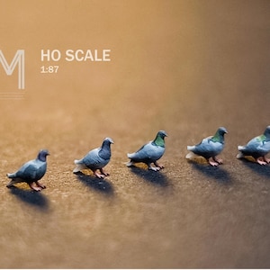 Op de afbeelding: Miniatuur HO-schaalmodelduiven. De vogels zijn geschilderd in tinten grijs, blauw en groen, met rode poten. De afbeelding bevat de tekst "HO SCALE 1:87" in het wit.