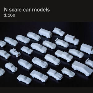 Può includere: Una collezione di modelli di auto bianche in scala N, scala 1:160, disposti su una superficie scura. I modelli includono vari tipi di auto, come berline, camion e furgoni. L'immagine include il testo "N scale car models" e "1:160".