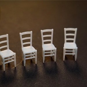 May include: Four miniature white chairs with ladder backs. The chairs have a classic design, with a seat and four legs. The background is a dark, neutral colour, which highlights the chairs. Each chair is approximately 3 cm in height.