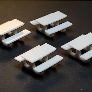 May include: Four miniature white picnic tables are arranged on a dark surface. Each table has a rectangular top and two attached benches. The tables are designed with rounded edges and a simple, clean aesthetic, perfect for a dollhouse or model scene.