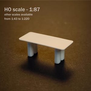 May include: A white miniature table with a rectangular top and two thick, rounded legs. The text on the image reads: M, HO scale - 1:87, other scales available from 1:43 to 1:220. This small model is designed for scale modeling projects.