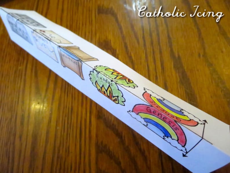 May include: A folded paper craft with illustrations of the books of Genesis and Exodus. The paper is white with colorful illustrations. The text "Genesis" and "Exodus" are visible.