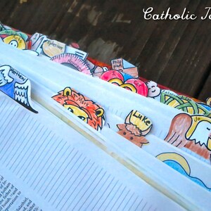 May include: A close-up of a Bible with colorful paper bookmarks. The bookmarks feature illustrations of animals and angels, with names like Matthew, Luke, and John.