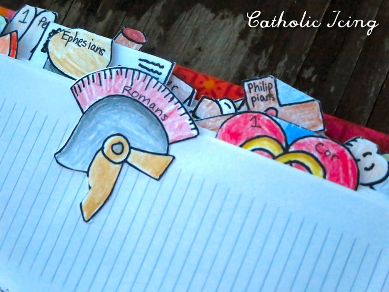 May include: A close-up of a notebook with colorful paper tabs sticking out. The tabs are labeled with different books of the Bible, including Romans, Ephesians, Philippians, and 1 Corinthians. The notebook is titled "Catholic Icing".