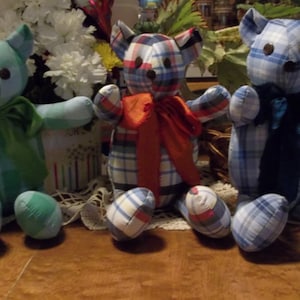 May include: Three plaid fabric teddy bears with different colored bows. The bear on the left is green and white, the middle bear is blue, white, and red, and the bear on the right is blue and white.