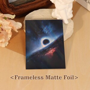 May include: A rectangular frameless matte foil print featuring a deep space scene with a central black hole surrounded by swirling blue and purple cosmic gases, light rays, and scattered dark debris against a dark, starry background.