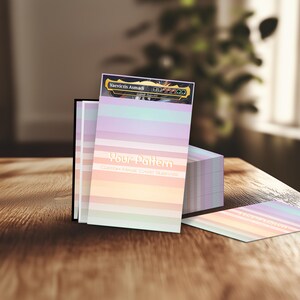 Puede incluir: Fundas de cartas personalizadas con un dise&ntilde;o de rayas de arco&iacute;ris pastel. El texto "Your Pattern" est&aacute; impreso en la parte delantera. La funda superior presenta el texto "Vaevictis Asmadi". Las fundas se muestran sobre una superficie de madera.