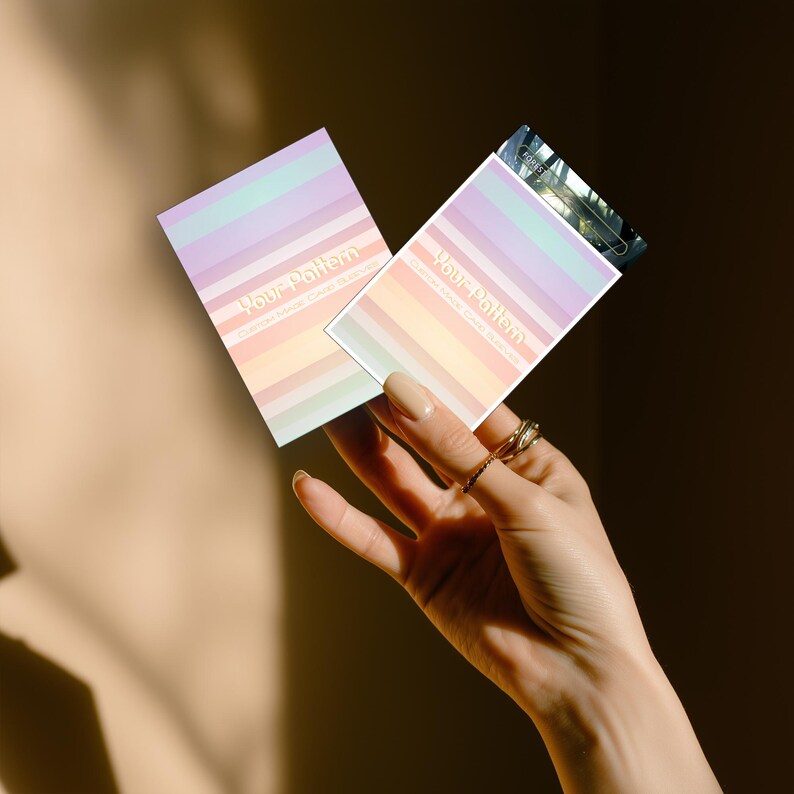 Puede incluir: Dos tarjetas rectangulares con rayas de arco&iacute;ris pastel se sostienen en una mano. Las tarjetas tienen el texto "Your Pattern" en una fuente de escritura. Las tarjetas est&aacute;n en orientaci&oacute;n vertical. El fondo es de un tono c&aacute;lido y neutro.