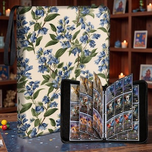 May include: A black card binder with a floral design and a matching carrying case. The case and binder feature a cream background with blue flowers and green leaves. The binder is open, displaying multiple trading cards.