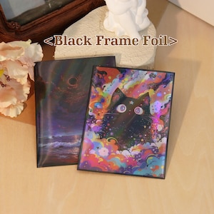 May include: Two rectangular prints with black frames labeled <Black Frame Foil>. One print features a dark ocean scene with a black sun, while the other displays a black cat surrounded by vibrant, multicolored clouds and stars with a foil finish.