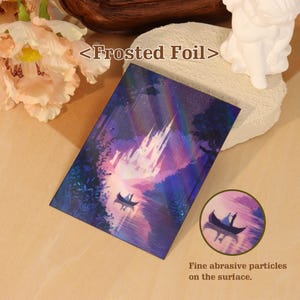 May include: A rectangular card featuring a Frosted Foil finish with a dark purple and blue illustration of a castle at night, a boat on water, and a rainbow holographic effect. The text <Frosted Foil> and Fine abrasive particles on the surface appear.