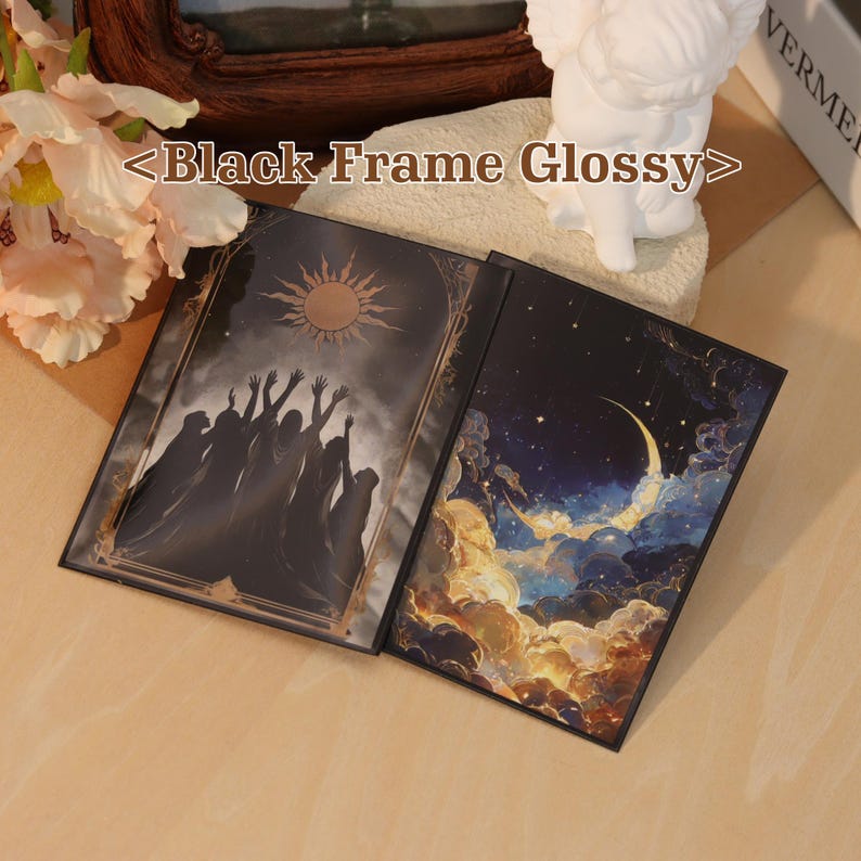 May include: A glossy black frame containing two rectangular art prints. The left print depicts silhouettes of figures reaching toward a sun in a dark sky. The right print shows a crescent moon surrounded by glowing clouds and stars in a night sky.
