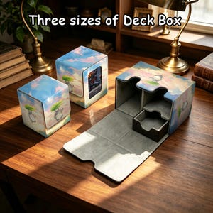 May include: Three deck boxes in different sizes featuring a light blue sky and cloud print with a small grey creature illustration. The boxes have a smooth exterior and a grey interior lining. The text "Three sizes of Deck Box" is visible.