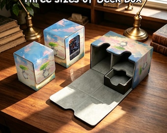 Op de afbeelding: Drie deckboxen in verschillende maten met een lichtblauwe lucht- en wolkenprint en een illustratie van een klein grijs wezen. De boxen hebben een gladde buitenkant en een grijze binnenvoering. De tekst "Three sizes of Deck Box" is zichtbaar.