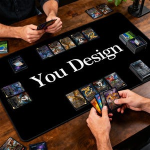 May include: A black gaming mat with the text "You Design" in white. The mat is covered with trading cards, with hands holding and arranging the cards. The cards have colorful illustrations and designs.