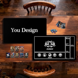 Op de afbeelding: Twee zwarte speelmatten met witte ontwerpen en tekst worden op een houten tafel getoond. Eén mat zegt "You Design" in het wit. De andere mat heeft een lotusbloemontwerp en het woord "Battlefield". Er liggen ook verschillende ruilkaarten en dobbelstenen op de tafel.