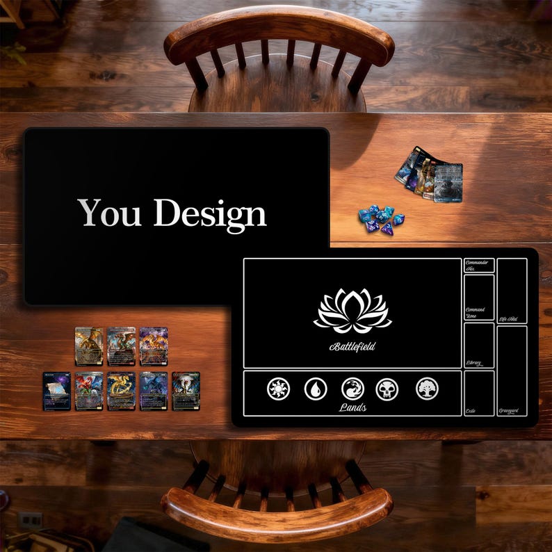 May include: Two black playmats with white designs and text are displayed on a wooden table. One mat says "You Design" in white. The other mat has a lotus flower design and the word "Battlefield". Several trading cards and dice are also on the table.