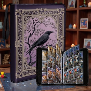 Op de afbeelding: Een donkerpaarse kaartenbinder met een ravenillustratie en gouden accenten. De binder is open en toont kaarthoesjes gevuld met kleurrijke ruilkaarten. Een zwarte draagriem is bevestigd.