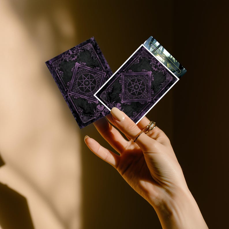 May include: Two rectangular playing cards featuring a dark charcoal background with intricate purple filigree borders and a central geometric star emblem. The cards display a gothic aesthetic with ornate detailing and a visible white edge border.