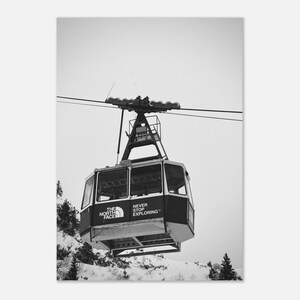 May include: Black and white image of a cable car with the text "THE NORTH FACE" and "NEVER STOP EXPLORING". The cable car is suspended by cables and is set against a snowy mountain backdrop.